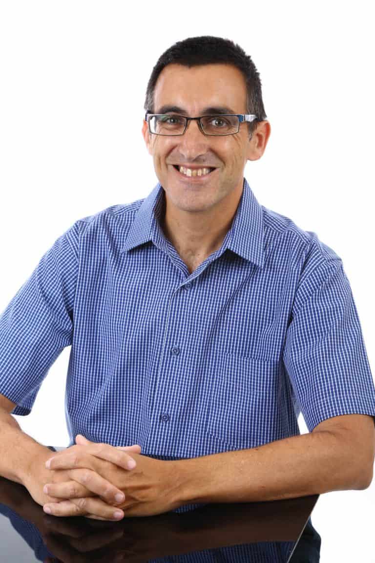 ארז שמש יועץ משכנתאות יושב משלב ידים ומחייך למצלמה